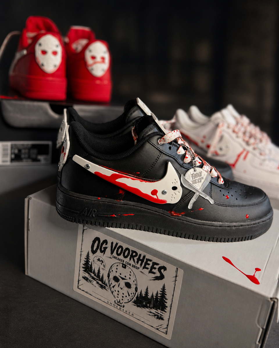A black Nike Air Force 1 sneaker with horror-themed graphics, including a white hockey mask Swoosh and red blood splatter details, displayed on top of a custom 'OG VOORHEES' shoebox. Other themed sneakers are visible in the background.