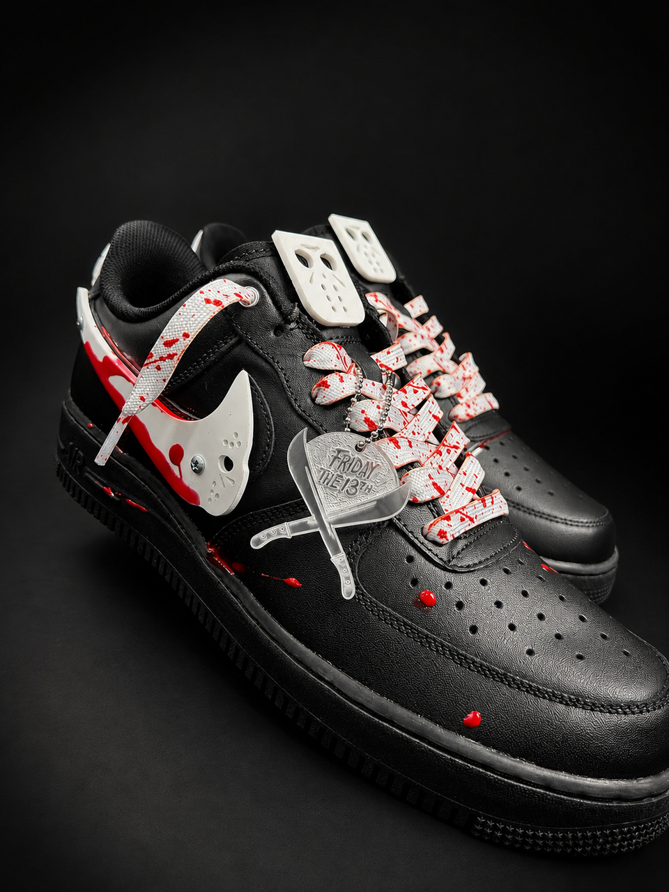 A pair of black Nike Air Force 1 Low sneakers with a horror-themed design, featuring red blood-splatter details, white laces printed with red splatters, and a clear plastic tag attached to the laces.