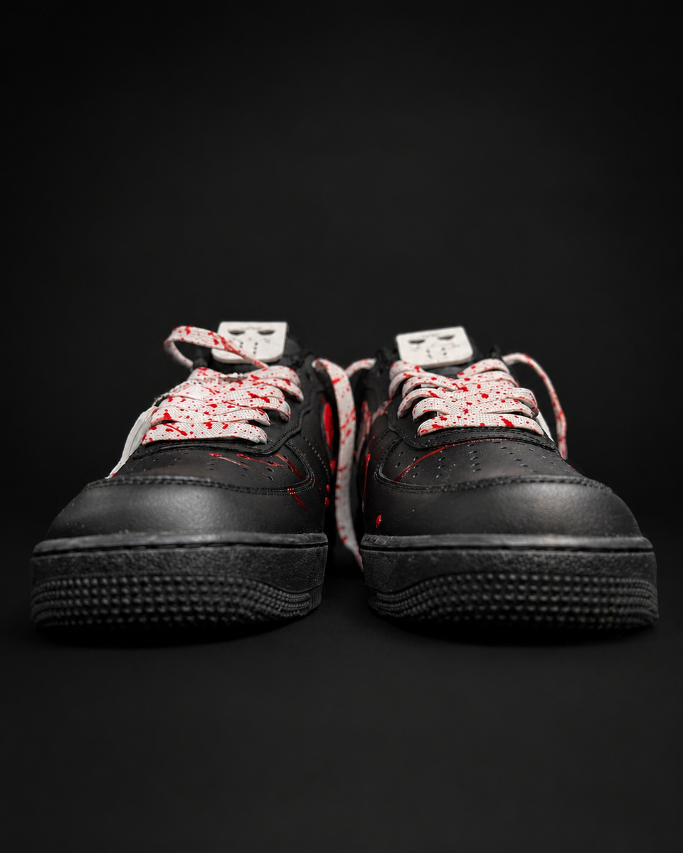 A pair of black low-top sneakers with white laces splattered in red, photographed against a solid black background.