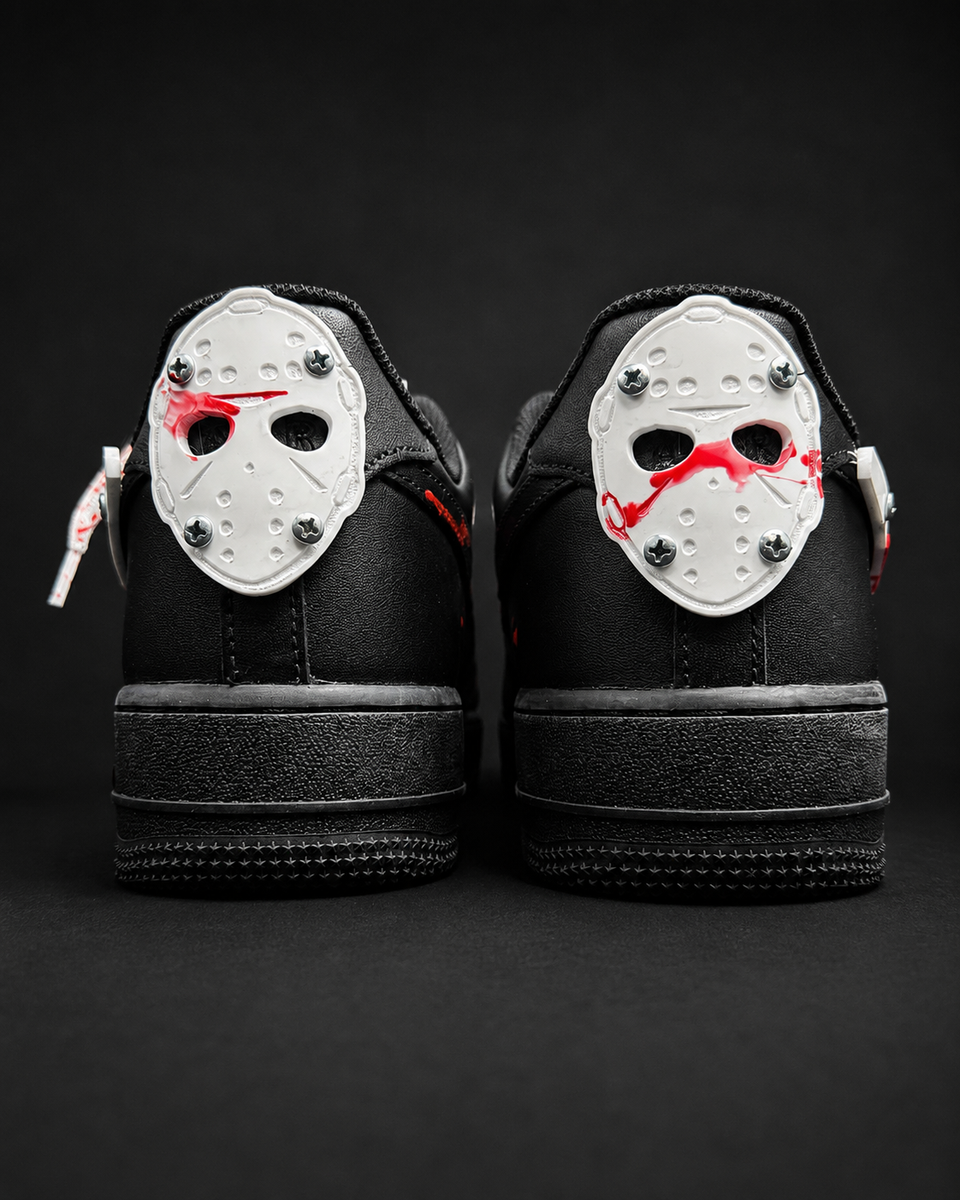 A pair of black low-top sneakers shown from the back, featuring a white hockey mask graphic with red blood splatter and silver studs on the heel counter.
